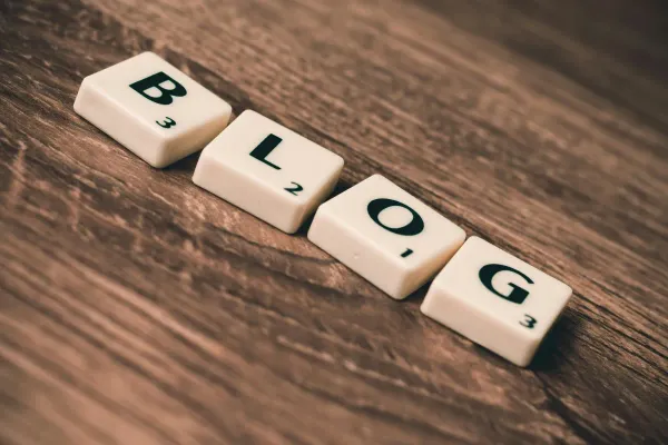 Photo of the word "Blog" spelt out in Scrabble pieces on wooden surface.