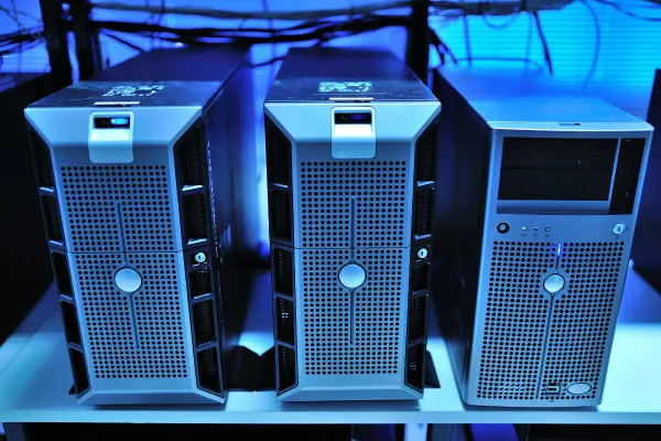 Three old-style tower PCs on a shelf, back-lit by blue light.