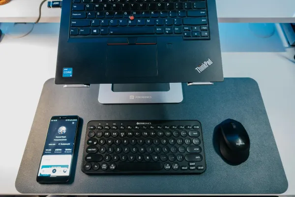 ThinkPad on a raised mount with only the keyboard portion in frame.  A phone, keyboard & mouse sits in front of the ThinkPad.